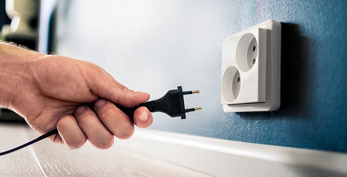 A hand connecting a cable to an electrical socket on the wall